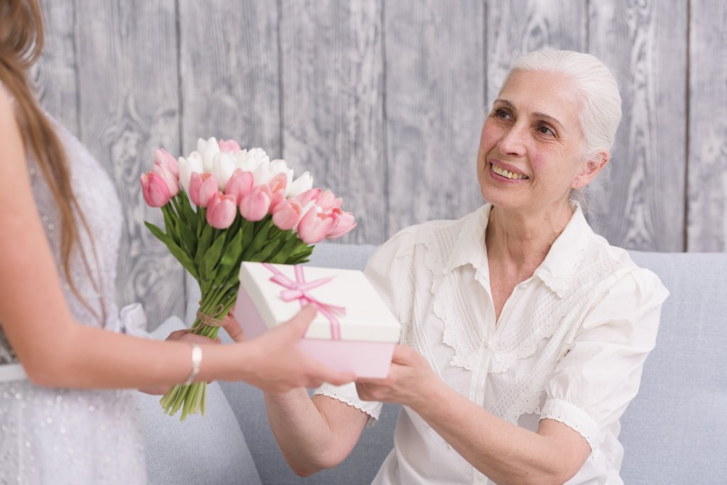 smiling-elder-woman-receiving-flower-bouquet-and-gift-box-front-her-grandchild.jpg
