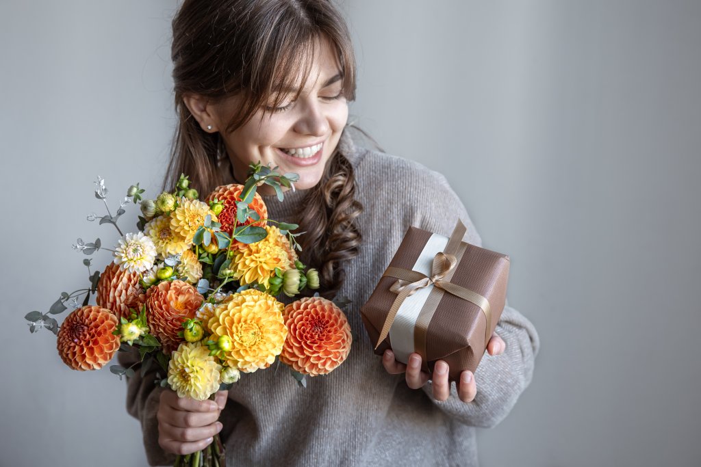 young-woman-with-a-gift-box-and-a-bouquet-of-flowers-in-her-hands.jpg
